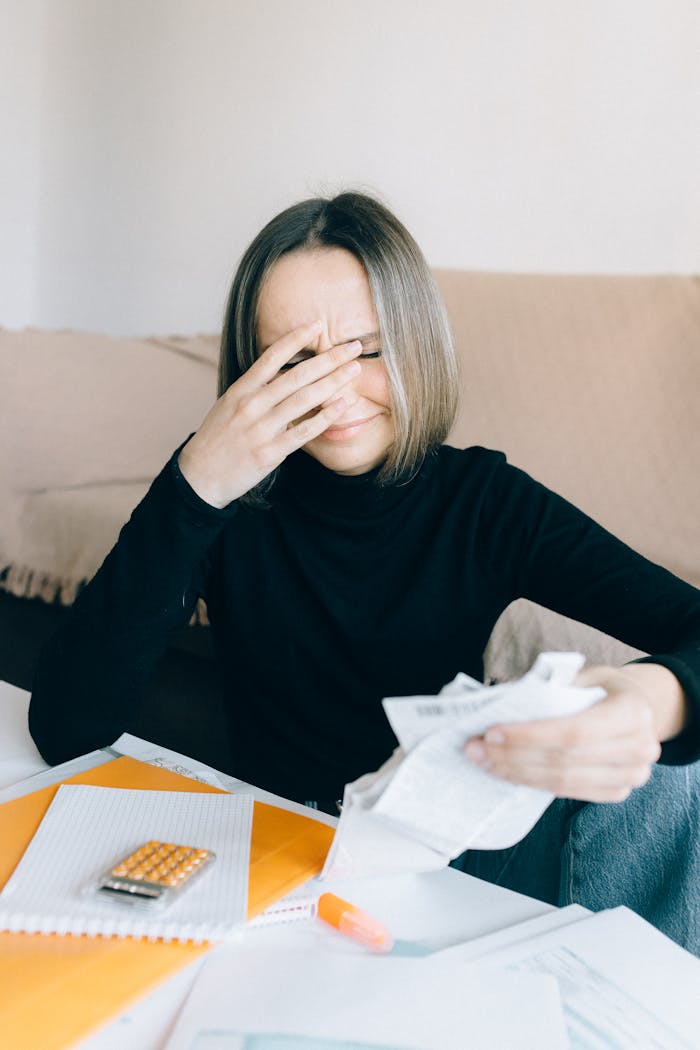 Young woman overwhelmed by bills and finances, holding receipts indoors.