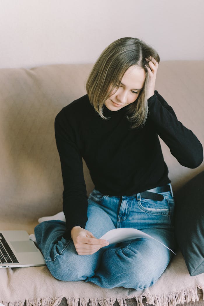 A young woman in casual attire appears stressed while reviewing a document indoors.